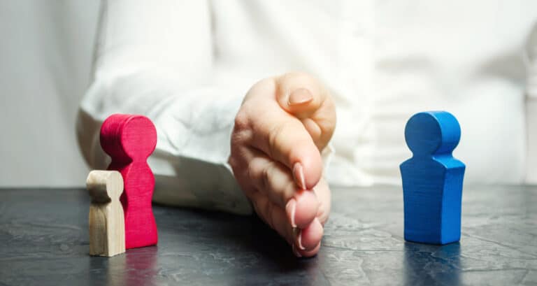 Wooden figures of two parents and a child separated by a hand, symbolizing child custody and support.