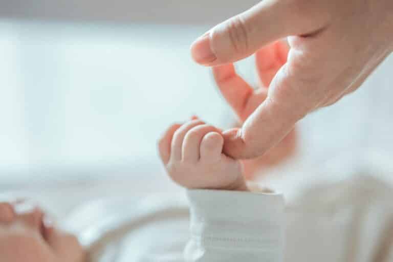 Close-up of a newborn baby holding an adult’s finger, symbolizing the connection between parent and child.