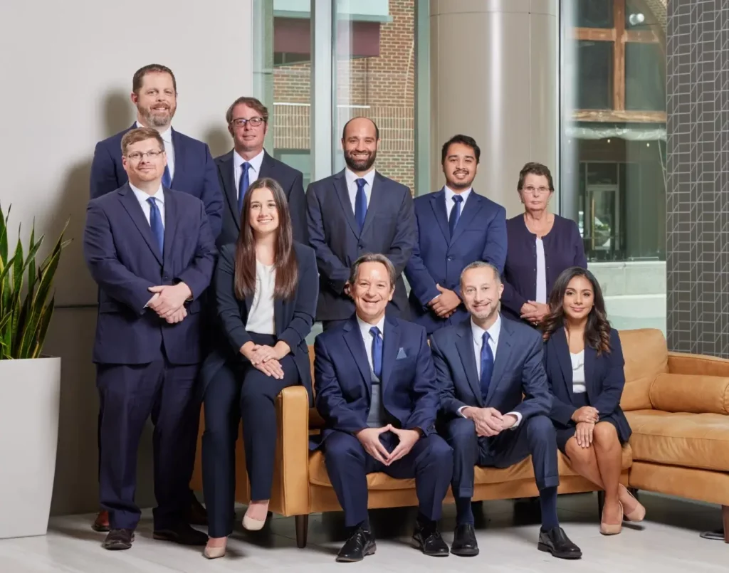 A group of nine professionals, dressed in formal business attire, posing together in a modern office setting