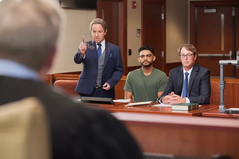 Defendant seated with two attorneys at the defense table in a courtroom