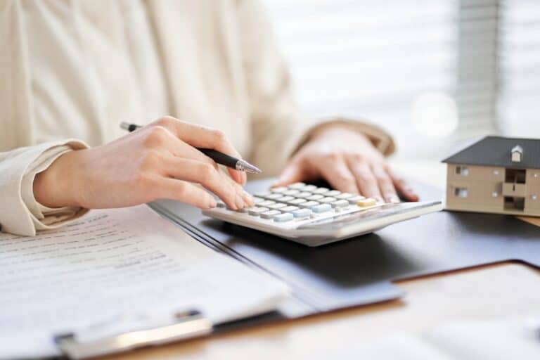 Close-up of a person using a calculator with documents and a model house on the desk, symbolizing asset division or financial planning during divorce.