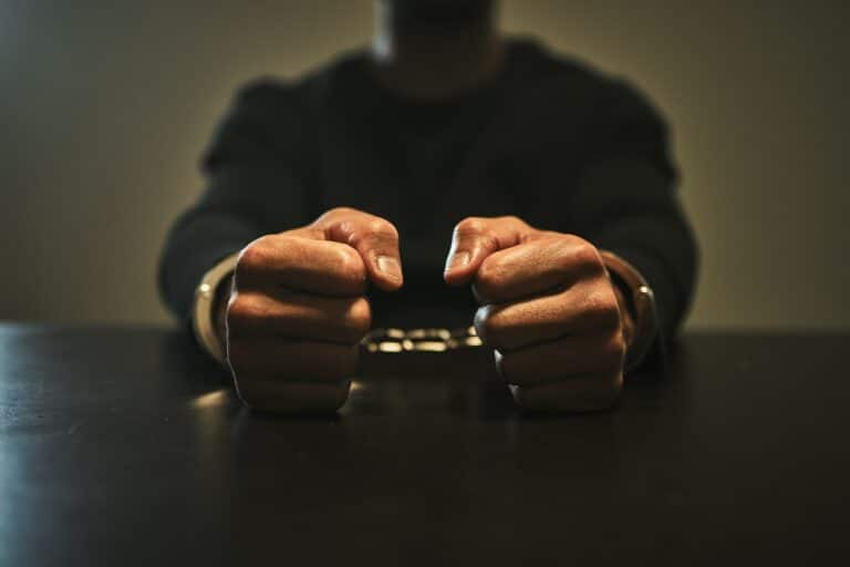 A man in an interview room, with a close-up on handcuffed hands ready for the police questioning.