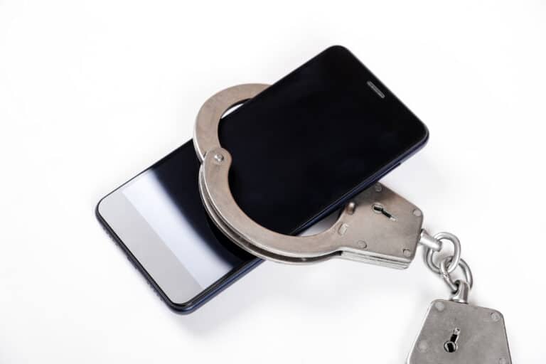 A close-up of a smartphone in handcuffs on a white background closeup