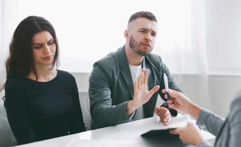 A couple meeting with a lawyer during a tense divorce or separation discussion, with the man gesturing to decline signing documents, symbolizing disagreement over legal or financial terms.